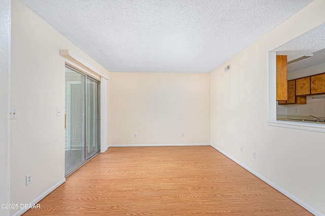 spare room featuring visible vents, baseboards, light wood-style flooring, and a textured ceiling