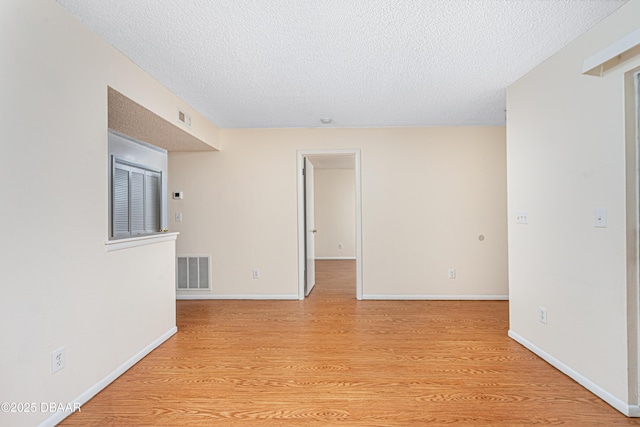 empty room with light wood-style floors, visible vents, a textured ceiling, and baseboards