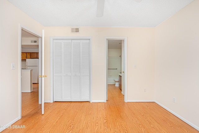 unfurnished bedroom featuring light wood finished floors, baseboards, visible vents, freestanding refrigerator, and a closet