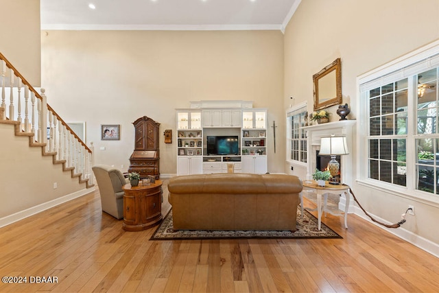 living room with a high ceiling, light wood-type flooring, and crown molding