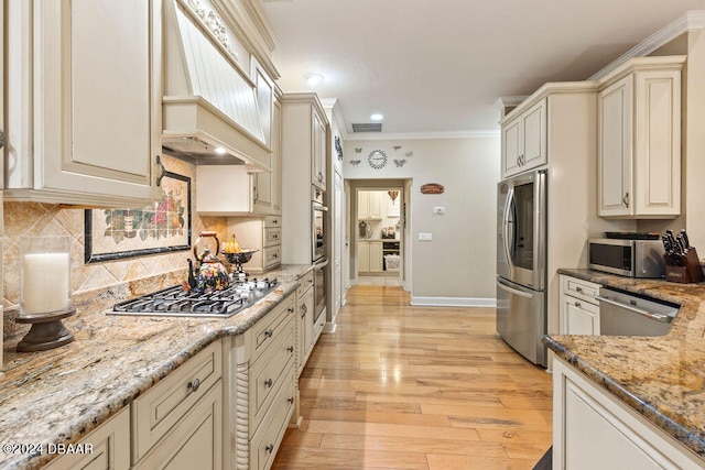 kitchen with light stone countertops, appliances with stainless steel finishes, crown molding, cream cabinets, and light hardwood / wood-style flooring