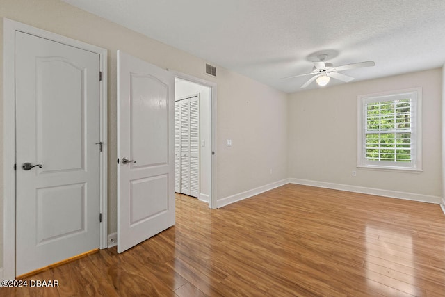 empty room with a textured ceiling, light wood-type flooring, and ceiling fan