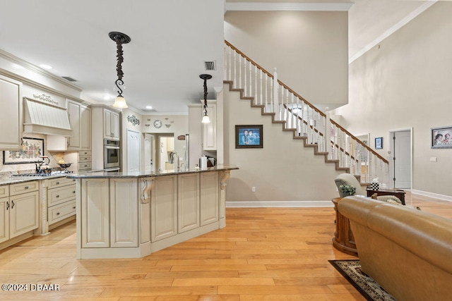 kitchen featuring light hardwood / wood-style flooring, light stone countertops, appliances with stainless steel finishes, cream cabinetry, and decorative light fixtures