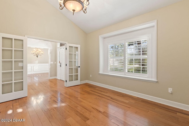 unfurnished room with french doors, high vaulted ceiling, hardwood / wood-style flooring, and an inviting chandelier