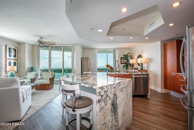 kitchen with stainless steel appliances, a large island with sink, sink, light stone countertops, and dark wood-type flooring