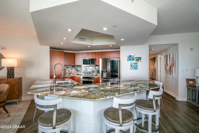 kitchen featuring light stone counters, appliances with stainless steel finishes, a kitchen bar, dark hardwood / wood-style flooring, and sink