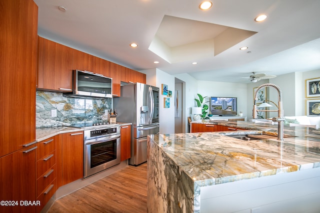 kitchen with stainless steel appliances, light hardwood / wood-style floors, extractor fan, kitchen peninsula, and decorative backsplash