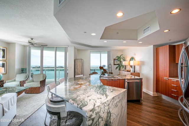 kitchen with light stone counters, a large island with sink, dark wood-type flooring, a water view, and ceiling fan