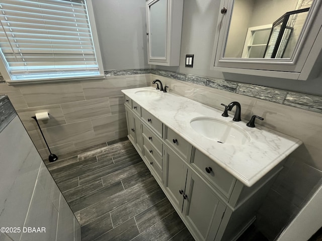 full bath with wood finish floors, a sink, tile walls, and double vanity