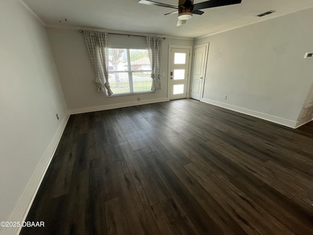 empty room featuring baseboards, visible vents, dark wood finished floors, and crown molding