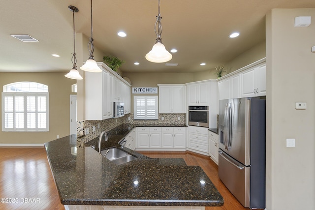 6065 Spruce Point Cir, Port Orange, FL 32128 - kitchen with appliances with stainless steel finishes, a peninsula, decorative backsplash, wood finished floors, and white cabinetry