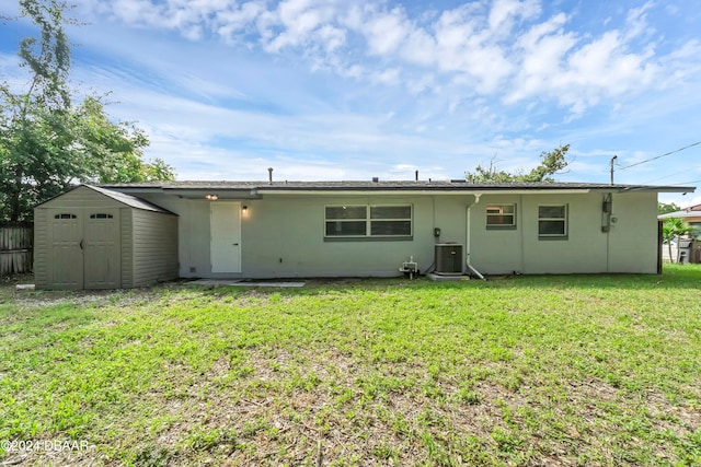 rear view of property featuring cooling unit, a storage unit, and a yard