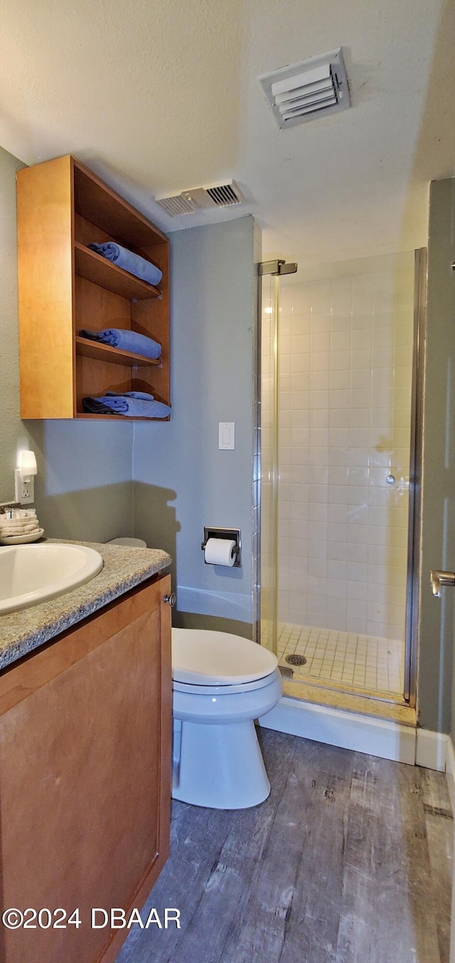 bathroom with hardwood / wood-style floors, vanity, toilet, and a shower with shower door