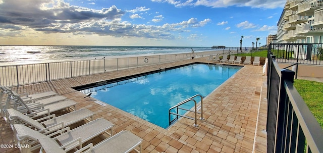 view of swimming pool with a patio, a beach view, and a water view