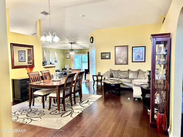 dining room featuring dark wood-style floors, visible vents, vaulted ceiling, and ceiling fan with notable chandelier