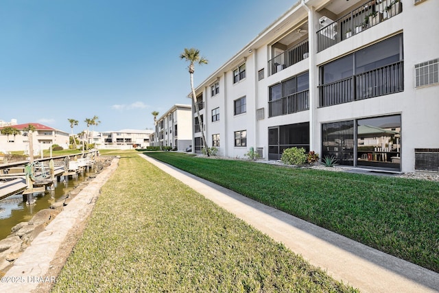 view of property's community featuring a water view, a boat dock, and a lawn