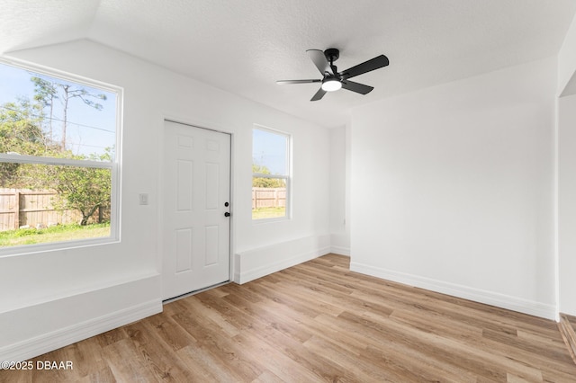 spare room featuring light wood-type flooring, plenty of natural light, a textured ceiling, and baseboards