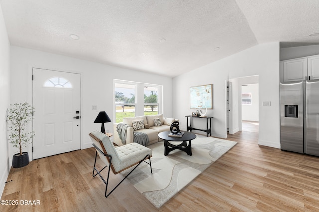 living area with lofted ceiling, light wood finished floors, a textured ceiling, and baseboards