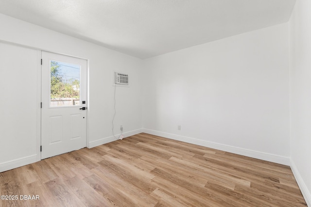 spare room featuring light wood-type flooring, a wall unit AC, and baseboards