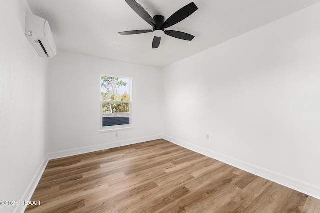 empty room with an AC wall unit, ceiling fan, baseboards, and wood finished floors