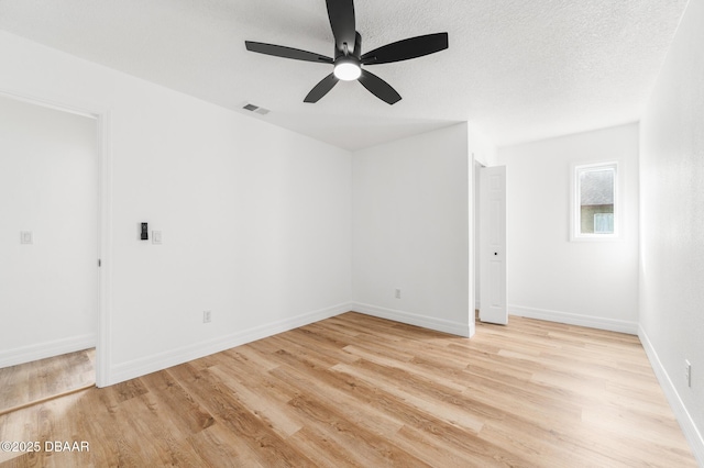 spare room featuring visible vents, light wood-style flooring, baseboards, and a textured ceiling