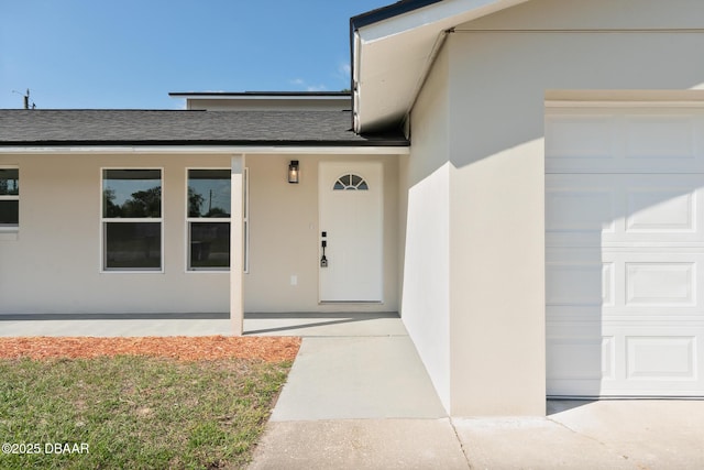 doorway to property featuring an attached garage, roof with shingles, and stucco siding