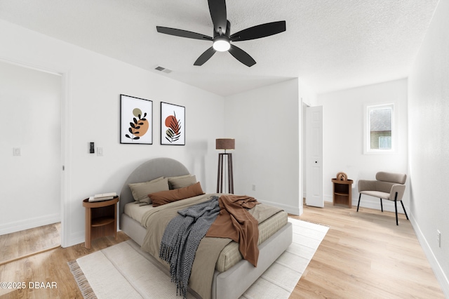 bedroom with a textured ceiling, baseboards, visible vents, and light wood-style floors