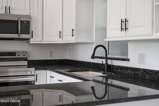 kitchen featuring white cabinetry, appliances with stainless steel finishes, dark stone counters, and a sink