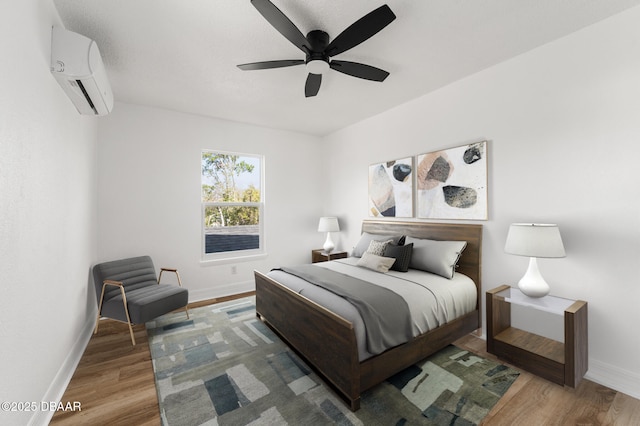 bedroom featuring a ceiling fan, wood finished floors, baseboards, and a wall mounted AC