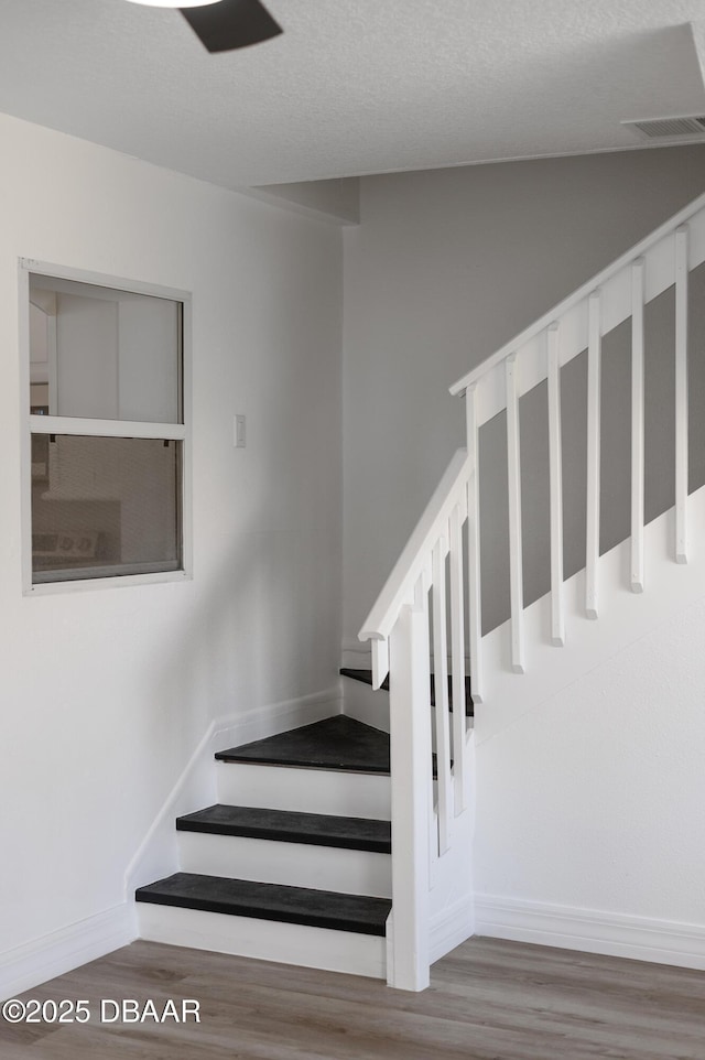 stairway with baseboards, a textured ceiling, visible vents, and wood finished floors