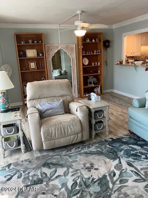 living room with wood-type flooring, a textured ceiling, ceiling fan, and ornamental molding