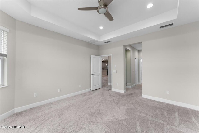 unfurnished bedroom featuring ceiling fan, light colored carpet, and a raised ceiling