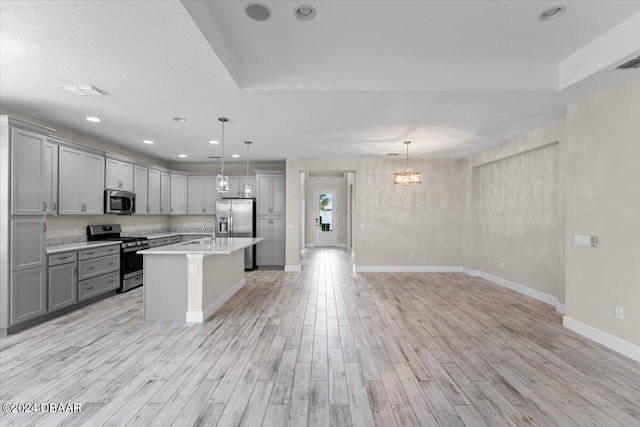 kitchen featuring a kitchen island with sink, gray cabinets, stainless steel appliances, and pendant lighting