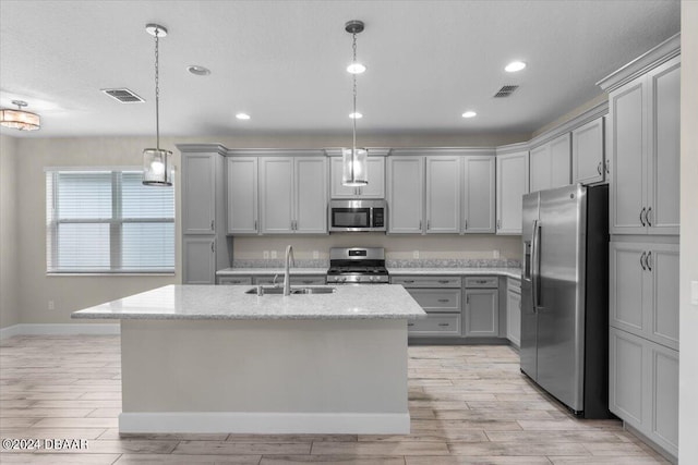 kitchen featuring decorative light fixtures, sink, appliances with stainless steel finishes, and a kitchen island with sink