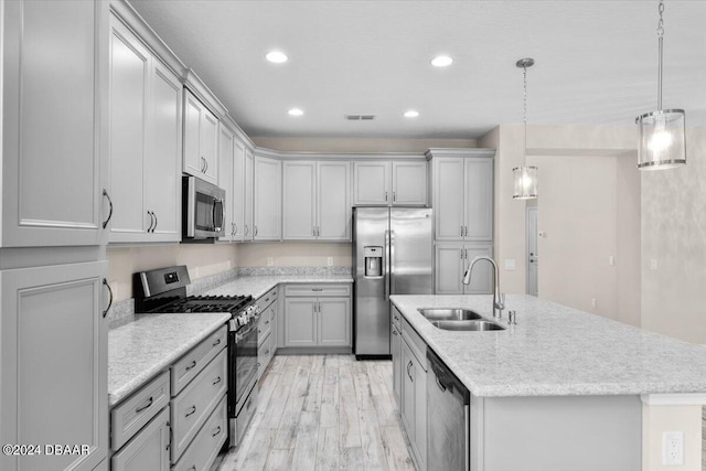 kitchen with an island with sink, appliances with stainless steel finishes, sink, and pendant lighting