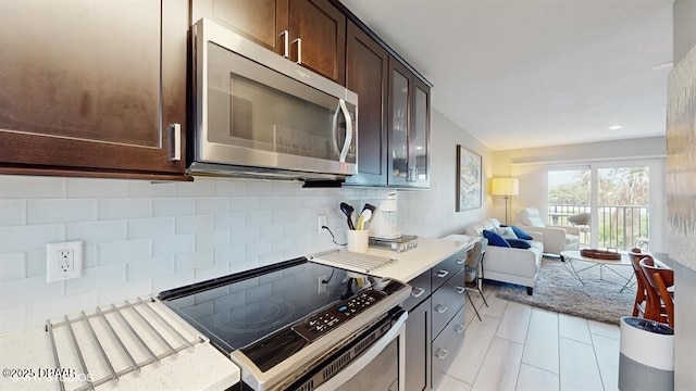 3170 Ocean Shore Blvd Unit 105, Ormond Beach, FL 32176 - kitchen with stainless steel appliances, tasteful backsplash, dark brown cabinetry, open floor plan, and glass insert cabinets