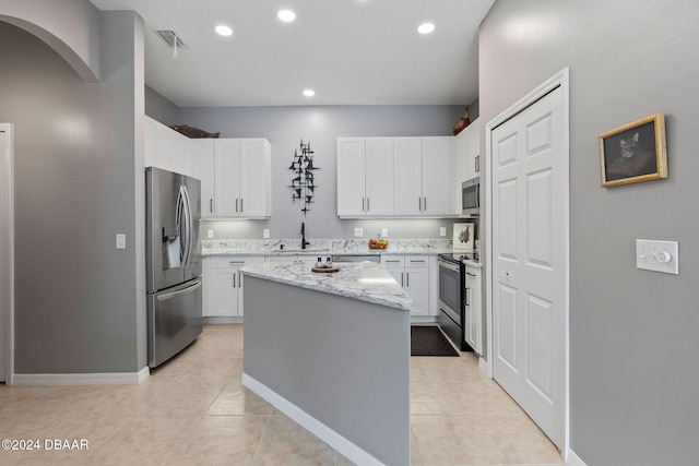 kitchen with a kitchen island, appliances with stainless steel finishes, light stone countertops, sink, and white cabinets