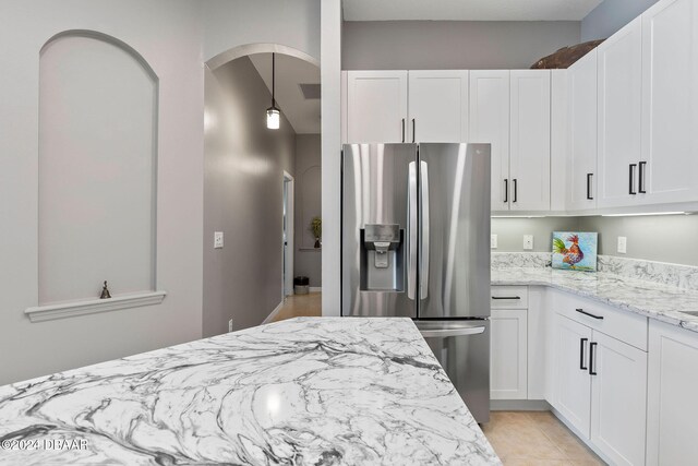 kitchen with white cabinets, light tile patterned floors, light stone countertops, decorative light fixtures, and stainless steel fridge