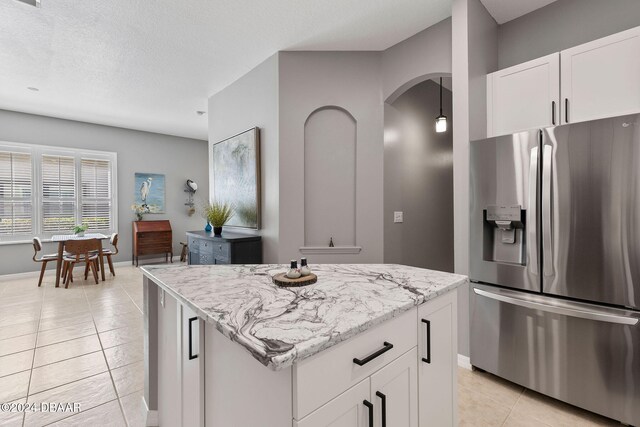 kitchen featuring light stone countertops, stainless steel fridge with ice dispenser, white cabinetry, and a kitchen island