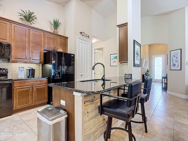 kitchen featuring dark stone counters, sink, black appliances, and high vaulted ceiling