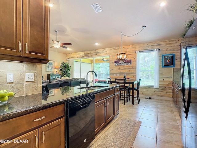 kitchen featuring wood walls, dark stone counters, plenty of natural light, and dishwasher