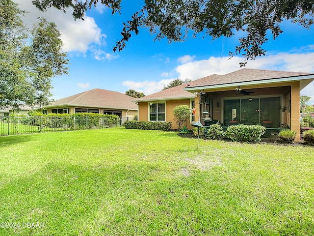 rear view of property featuring a sunroom, a lawn, and ceiling fan