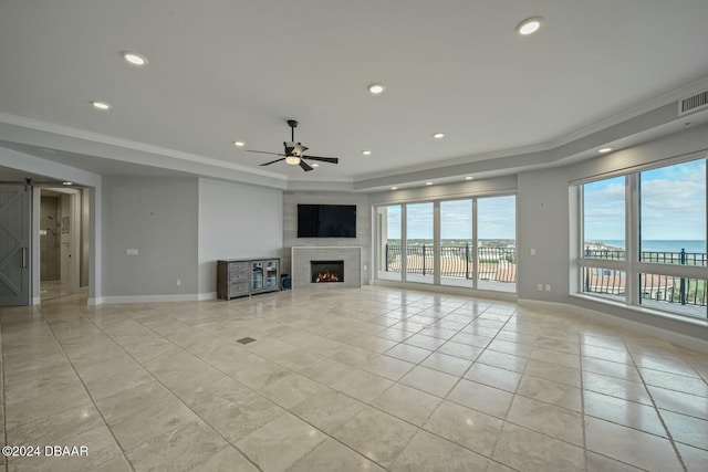 unfurnished living room with ceiling fan, a barn door, plenty of natural light, and ornamental molding