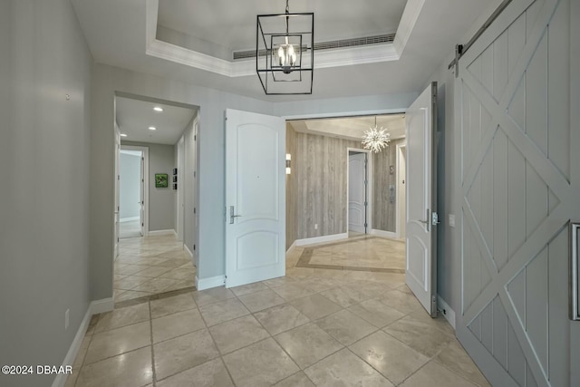 hallway with a raised ceiling, a barn door, ornamental molding, and an inviting chandelier