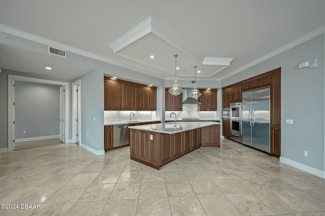 kitchen with appliances with stainless steel finishes, wall chimney exhaust hood, sink, a center island with sink, and decorative light fixtures