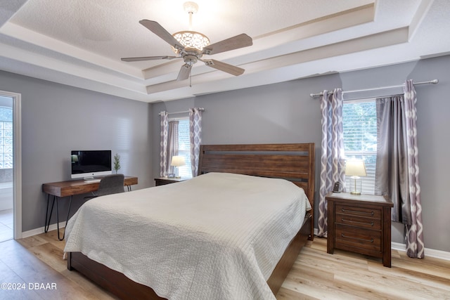 bedroom with ceiling fan, a raised ceiling, and light wood-type flooring