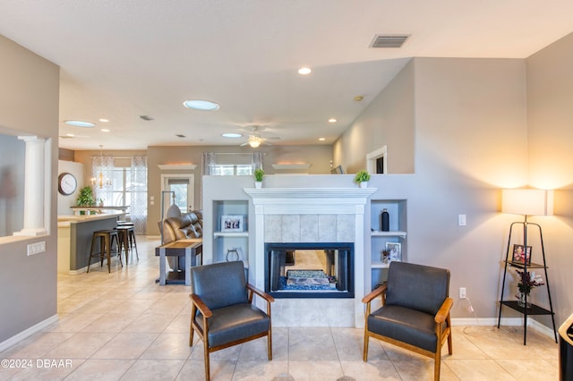 tiled living room with a fireplace, ceiling fan with notable chandelier, and decorative columns