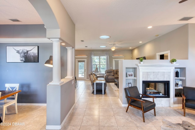 tiled living room featuring ceiling fan, decorative columns, and a tiled fireplace