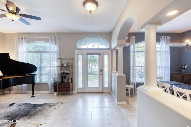 tiled entrance foyer with ceiling fan with notable chandelier, a healthy amount of sunlight, and decorative columns