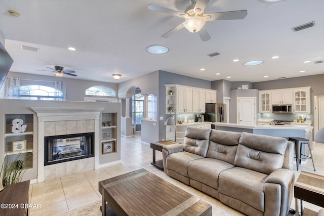 tiled living room featuring ceiling fan, a tile fireplace, a textured ceiling, and a wealth of natural light